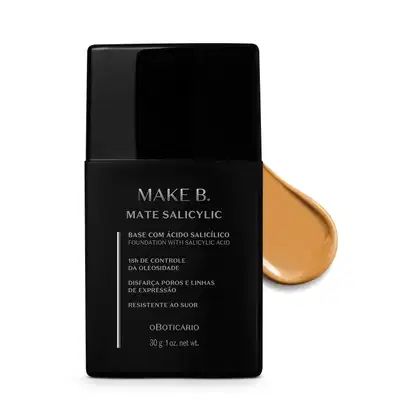 Frasco preto de base da linha Make B. Mate Salicylic com texto em branco trazendo informações do produto, como presença de ácido salicílico, controle de oleosidade e resistência ao suor. Atrás da embalagem, vemos um pouco de base bege média espalhada.