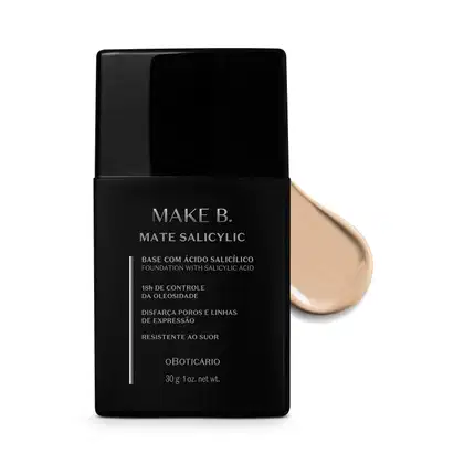 Frasco preto de base da linha Make B. Mate Salicylic com texto em branco trazendo informações do produto, como presença de ácido salicílico, controle de oleosidade e resistência ao suor. Atrás da embalagem, vemos um pouco de base bege clara espalhada.