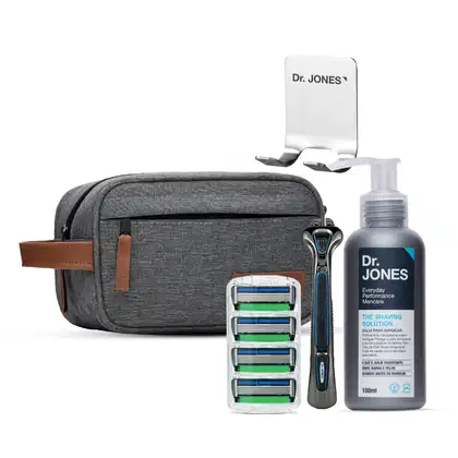 Estojo de viagem cinza com produtos de barbear da marca Dr. Jones, incluindo bálsamo para barba, aparelho de barbear e lâminas de reposição. O estojo possui bolsos e detalhes em couro.