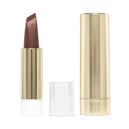 Na imagem o Batom Eudora Glam Amulips na cor Marrom Determinado, um tom de marrom elegante. O batom está aberto, revelando seu interior com o nome Eudora gravado no produto. A embalagem dourada transmite a elegância e qualidade do produto.