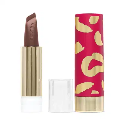 Na imagem há a case de um batom. Ela tem um padrão de manchas abstratas em rosa vibrante e dourado metálico. Esse design moderno e sofisticado com cores vivas é característico de uma linha de cosméticos glam e de luxo.