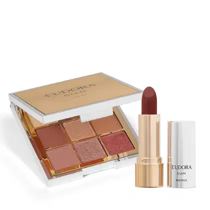 Paleta com embalagem compacta retangular de plástico cromado com espelho interno. Batom cremoso de cor marrom intenso em embalagem dourada cilíndrica.  Ao lado, está a tampa na cor prata. Ambos possuem "Eudora Glam Metals" escrito no logo em preto.