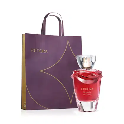 A imagem mostra desodorante colônia Eudora Magnific Rouge Camélia em frasco de vidro vermelho transparente e uma sacola retangular roxa com detalhes dourados e o logotipo Eudora em letras maiúsculas. Cores predominantes são vermelho, roxo e dourado.