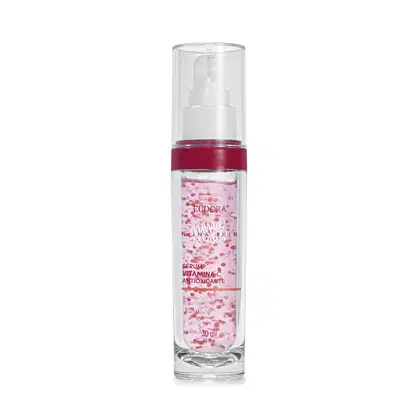 A imagem mostra um frasco pequeno, cilíndrico, transparente com tampa também transparente, visto de frente. O rótulo tem fundo rosa claro com detalhes em vermelho, exibindo o nome do produto, marca e volumetria com letras rosa e branca,