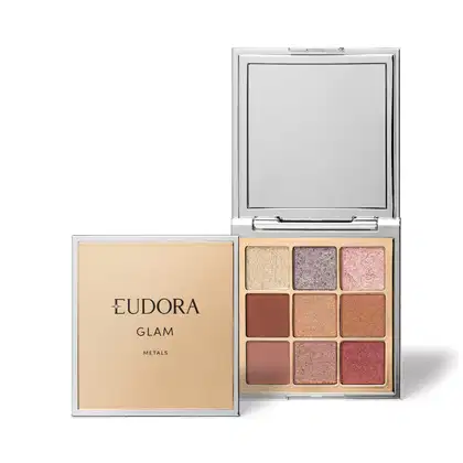 Embalagem compacta retangular de plástico cromado com espelho interno. A caixa externa é bege com o logotipo "Eudora Glam Metals" em letras douradas. Contém 9 sombras prensadas em tons terrosos, rosas, marrons e dourados com acabamento metálico brilhante.