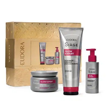 A imagem mostra produtos da linha Glow Expert da marca Siàge e caixa dourada com detalhes geométricos em relevo. Contém shampoo de 250ml, máscara  de 250g e um leave-in de 100ml. Embalagens plásticas com detalhes em vermelho e prata.