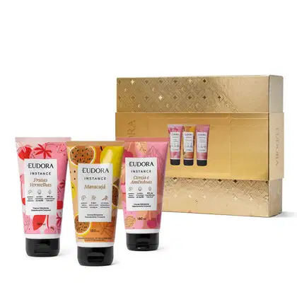 A imagem mostra uma caixa dourada decorada  e três hidratantes Eudora da linha Instance, com as fragrâncias Frutas Vermelhas, Maracujá e Cerejas e Amêndoas, em embalagens coloridas em tons de vermelho, laranja e rosa.