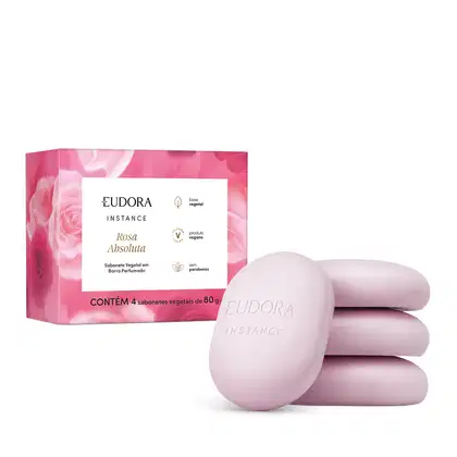 O produto apresentado é um conjunto de sabonetes vegetais da linha Instance Rosa Absoluta. A embalagem é uma caixa rosa com detalhes em branco, contendo 4 sabonetes vegetais de 80g cada. Os sabonetes em si possuem formato oval e coloração rosa clara.