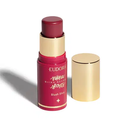 Blush em bastão Eudora Niina Secrets Daily, destampado com a tampa ao lado. Cor rosa com tampa dourada.
