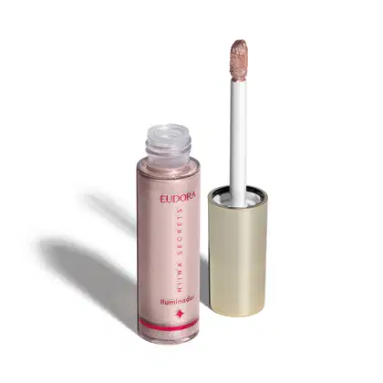 O produto apresentado é um iluminador da marca Eudora, da linha Niina Secrets. Trata-se de um frasco contendo um produto de cor rosé. O rótulo exibe o nome da marca "Eudora" e a descrição "Iluminador" em rosa. O aplicador é um pincel branco.