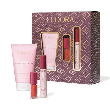 O conjunto de produtos Eudora apresentado inclui uma loção hidratante corporal, uma máscara para cílios e um gloss labial da linha Niina Secrets de Eudora. Junto, temos uma embalagem composta por uma caixa com padrões geométricos em tons de roxo e dourado