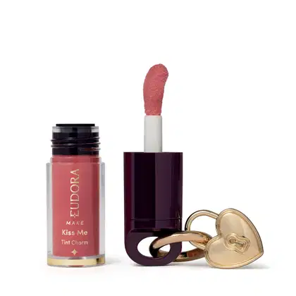 O produto de beleza Eudora Make apresenta um batom líquido rosa em embalagem cilíndrica, acompanhado de um espelho compacto dourado em formato de coração.