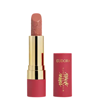 Batom rosa-coral com textura aveludada em embalagem dourada com detalhes florais, marca Eudora impressa em vermelho.
