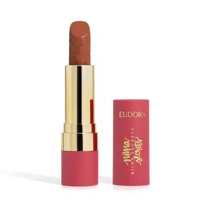 Embalagem de um batom aberto, com corpo dourado e tampa e base rosa, escrito "Eudora Niina Secrets". A cor do batom é castanho e tem um relevo exclusivo em padrão floral na bala. Produto de beleza com design elegante e sofisticado.