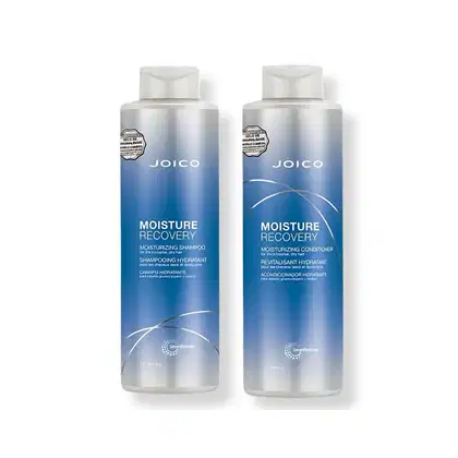 Dois frascos de produtos Joico da linha Moisture Recovery, um shampoo e um condicionador hidratantes, com embalagens em tons de azul e branco, apresentando rótulos com o nome da marca e da linha.