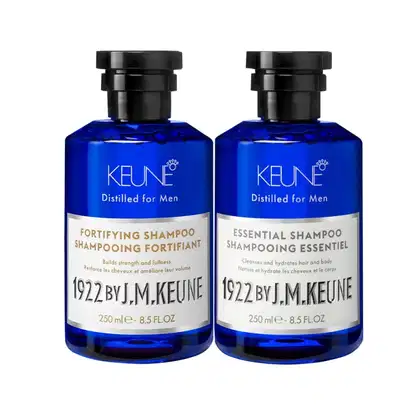 Dois frascos de shampoo da marca Keune, um de fortalecimento e outro essencial, em embalagens azuis com rótulos em branco e preto, contendo 250 ml cada.