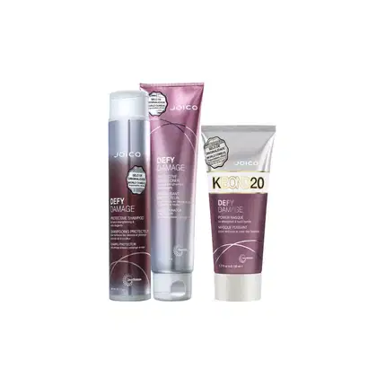 Produtos da linha Defy Damage da Joico, incluindo shampoo protetor, condicionador e máscara capilar, em embalagens com cores predominantes de rosa e cinza.