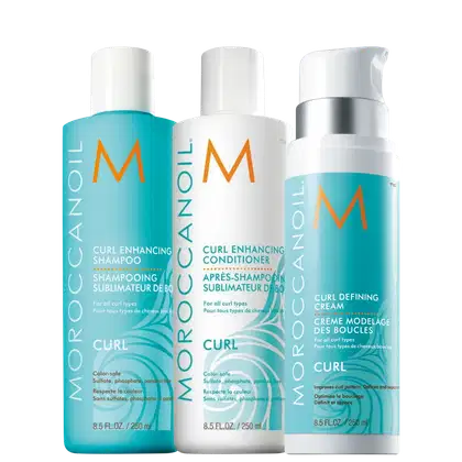 Produtos para cabelos cacheados da linha Moroccanoil Curl. Três embalagens plásticas cilíndricas: um shampoo de 250ml, um condicionadorde 250ml e um creme modelador de cachos de 250ml. As cores predominantes são azul claro, branco e laranja.