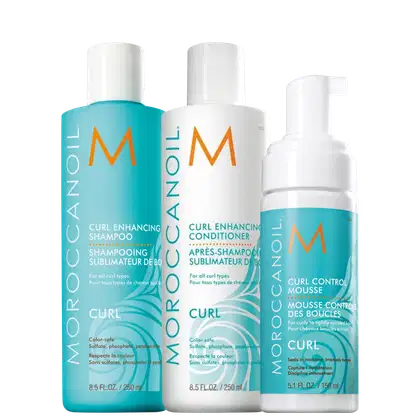 Produtos para cabelos cacheados da marca Moroccanoil. Inclui um shampoo de 250ml, um condicionador de 250ml e uma mousse capilar de 150ml. Todos os frascos têm o logotipo "M" laranja da marca. As cores predominantes são turquesa, branco e laranja.