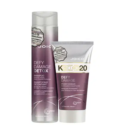 Shampoo e máscara capilar da linha Defy Damage Detox da marca Joico. O shampoo vem em um frasco cilíndrico branco com detalhes em roxo.  A máscara capilar é apresentada em um tubo branco com detalhes roxos.