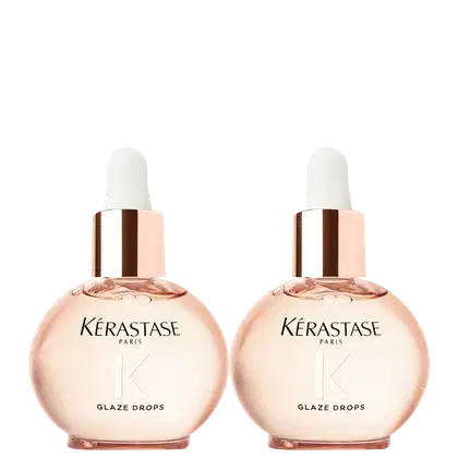 Dois frascos de vidro rosados da marca Kérastase Paris, contendo o produto Glaze Drops. Os frascos possuem um conta-gotas e uma tampa dourada, com o logotipo da marca claramente visível.