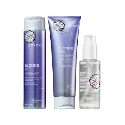 Produtos da linha Blonde Life da Joico: shampoo violeta, condicionador violeta e óleo brilhante em embalagens plásticas e tubulares de cores roxas e brancas.