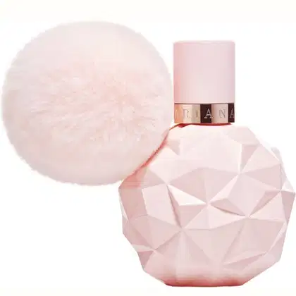 Frasco de perfume Ariana Grande em formato geométrico rosa, com tampa rosada e detalhes em metal dourado. Acompanha um elemento decorativo esférico e felpudo em tons de rosa.
