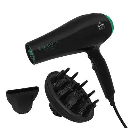 A imagem mostra um secador de cabelo profissional da marca GA.MA Italy. Ele possui um corpo cilíndrico preto com detalhes em verde escuro. Acompanha um difusor removível preto com pinos para modelar o cabelo e um bico de ar na cor preta.