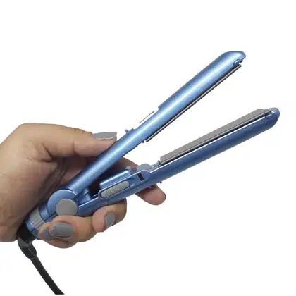 A imagem mostra uma mão segurando a chapinha, que é pequena na cor azul metálico com detalhes cinza.