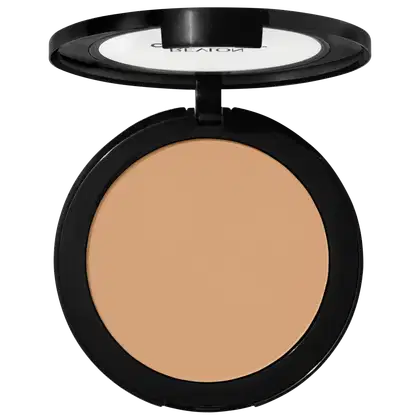 Pó compacto de maquiagem Revlon em embalagem redonda preta. A superfície do pó tem uma cor bege claro uniforme. A tampa transparente exibe o logotipo "Revlon" em letras brancas. O produto apresenta um design minimalista e elegante.