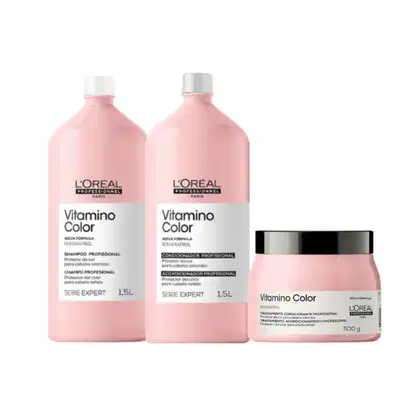 A imagem mostra três produtos da linha Vitamino Color da L'Oréal Professionnel. Dois frascos plásticos de 1,5 litros e um de 500g. Todos na cor rosa claro, com rótulos brancos e letras pretas.