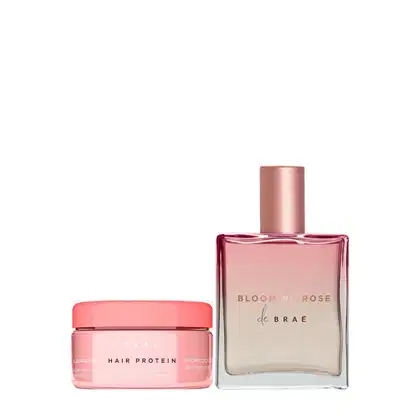 A imagem mostra dois produtos de beleza da marca Braé. Um é um frasco de perfume retangular de vidro rosa com uma tampa rosa metálica. O outro produto é um pequeno pote rosa com tampa da mesma cor, que contém um creme ou tratamento capilar.