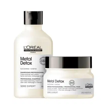 A imagem mostra dois produtos lado a lado. Um shampoo em frasco plástico branco com tampa preta, contendo 300ml. Uma máscara capilar em pote branco com tampa preta, com 250ml. Ambos têm rótulos escritos "Metal Detox" e "Glucoamine + Ionene" em preto.
