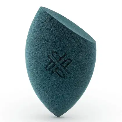 Esponja de maquiagem com textura aveludada na cor verde-azulada e logotipo impresso em preto. Produto da marca Petrizi Makeup, projetado para aplicação e mistura suave de maquiagem.