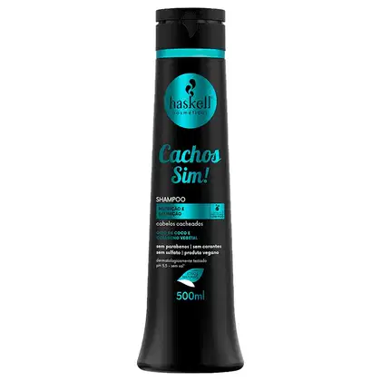 Shampoo da marca Haskell, chamado "Cachos Sim!". A embalagem contém informações sobre o produto, como "Nutrição e Definição" e "Óleo de Coco e Colágeno Vegetal". O frasco possui um formato cilíndrico e uma tampa preta. O tamanho do produto é de 500ml.