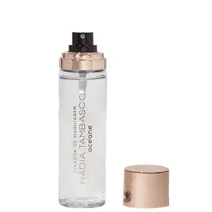 A imagem mostra o frasco do fixador de maquiagem aberto com a tampa ao lado, é uma embalagem transparente e cilíndrica, com o nome da marca e o texto "Océane" gravados nele. A tampa é de cor rosé gold e as letras do rótulo são douradas.