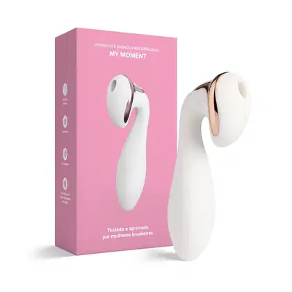 O produto apresentado é um vibrador e sugador recarregável chamado "My Moment", em uma caixa rosa. O dispositivo é branco com detalhes em rosa dourado, com um formato ergonômico e compacto.