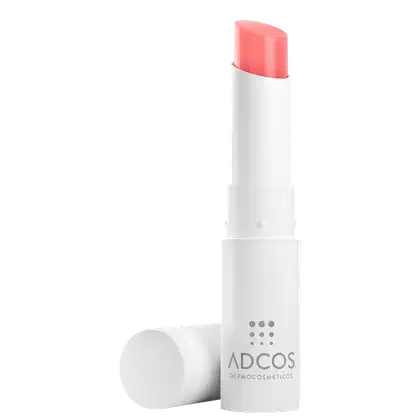 Hidratante labial em formato de bastão com embalagem cilíndrica branca. Na parte superior aparece um pedaço da bala do hidratante na cor coral. O corpo da embalagem apresenta o logotipo "ADCOS" impresso em letras cinza.