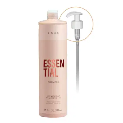 Shampoo Brae Essential em embalagem plástica rosa claro de 1 litro ou 33,8 fl oz. A embalagem tem o nome do produto "Essential" em letras grandes vermelhas e "Shampoo" abaixo em letras menores.
