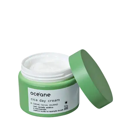 A imagem mostra a embalagem do creme hidratante facial Océane Cica Day Cream. O produto vem em um pote de plástico na verde com um rótulo branco e letras pretas descrevendo nome, marca e ativos. A embalagem está aberta com a tampa reclinada ao pote.
