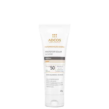 Protetor solar mousse mineral da marca Adcos, embalagem tubular branca. Rótulo com o nome do produto "Protetor Solar Mousse Mineral Nude" e informações como FPS 50, fator de proteção UVB e UVA 17. Embalagem de 40g.