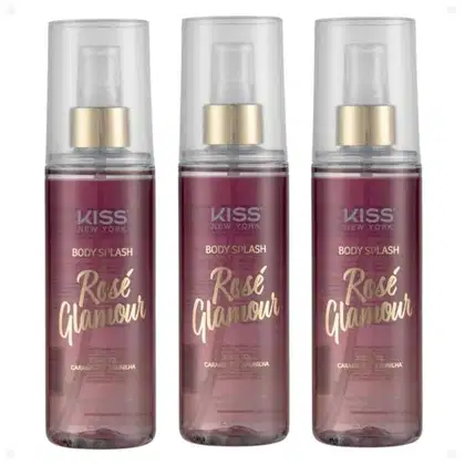 São três frascos de body splash da marca Kiss New York. Os frascos são cilíndricos, transparentes. O líquido é de cor rosé. Nas embalagens, está escrito "Body Splash Rose Glamour" em letras douradas.