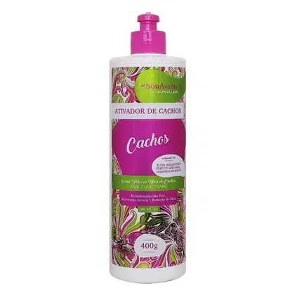 Ativador de cachos da linha #SouAssim da Alpha Line. Embalagem plástica branca e rosa com detalhes florais em verde e rosa. Rótulo em português indicando "Ativador de Cachos" e "Cachos" em letras grandes. I