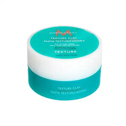 A imagem mostra o produtos Moroccanoil Texture Clay 75g, em embalagem plástica redonda na cor turquesa com detalhes em laranja e branco. No topo, há um rótulo com o nome do produto "Texture Clay" e a descrição "Pasta Texturizadora" em inglês e português.