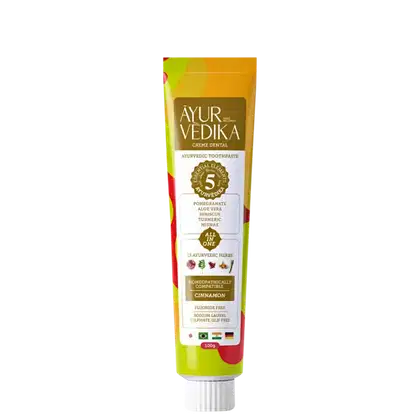 Creme dental Ayurvédico da marca Ayur Vedika. A embalagem é um tubo de cor amarela e laranja, com rótulos que destacam os ingredientes naturais utilizados, como romã, aloe vera, cúrcuma e 23 ervas ayurvédicas.