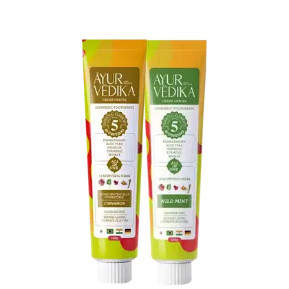 Dois tubos de creme dental, um com sabor de canela e outro de menta selvagem. Ambos os tubos possuem rótulos verdes e amarelos, com informações sobre os ingredientes Ayurvédicos utilizados, como romã, aloe vera, hibisco e curcuma.