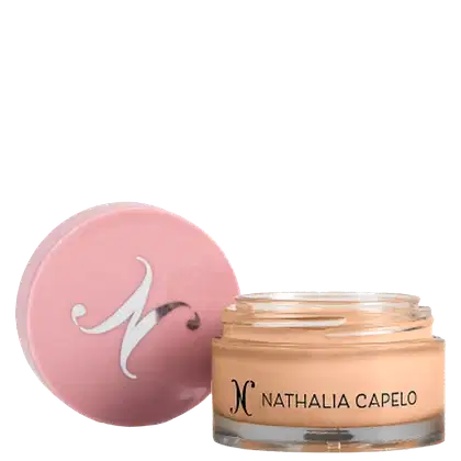 O produto apresentado é um item da marca Nathalia Capelo. Trata-se de um recipiente de vidro contendo corretivo para maquiagem. A embalagem é de cor rosa clara, com o logotipo da marca em destaque.