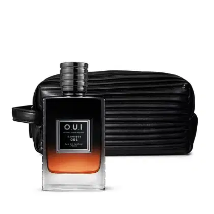A imagem mostra um frasco de vidro transparente com uma tampa preta sofisticada e um eau de parfum âmbar no seu interior. Ao está uma nécessaire texturizado em preto, ambos da marca O.U.i.