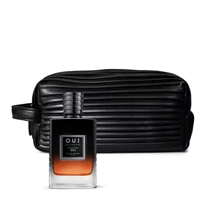 A imagem mostra um frasco de vidro transparente com uma tampa preta sofisticada e um eau de parfum âmbar no seu interior. Ao está uma nécessaire texturizado em preto, ambos da marca O.U.i.