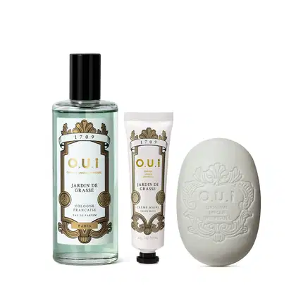 Conjunto de produtos de beleza da marca O.U.i., incluindo um frasco de perfume Jardin de Grasse, um tubo de creme para as mãos e um sabonete em forma de ovo com o logotipo da marca.